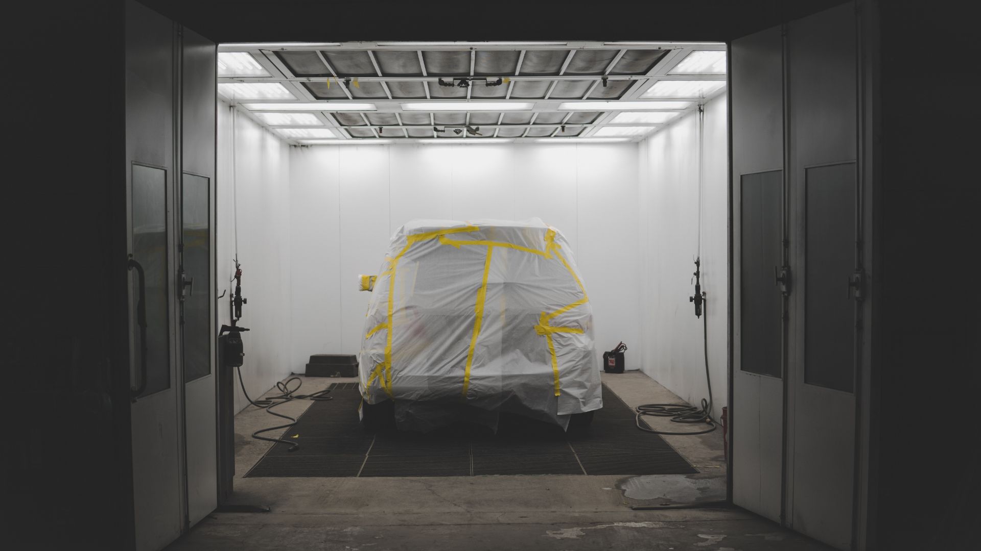 a car covered in a sheet in a garage.|a man painting a car in a garage.|a man working on a red truck in a garage.