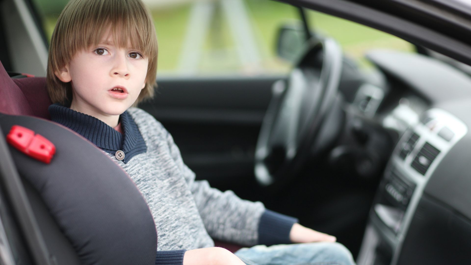 a young boy sitting in a car seat.|a woman sitting in a car looking at her cell phone.|a young girl sitting in a car using a cell phone.