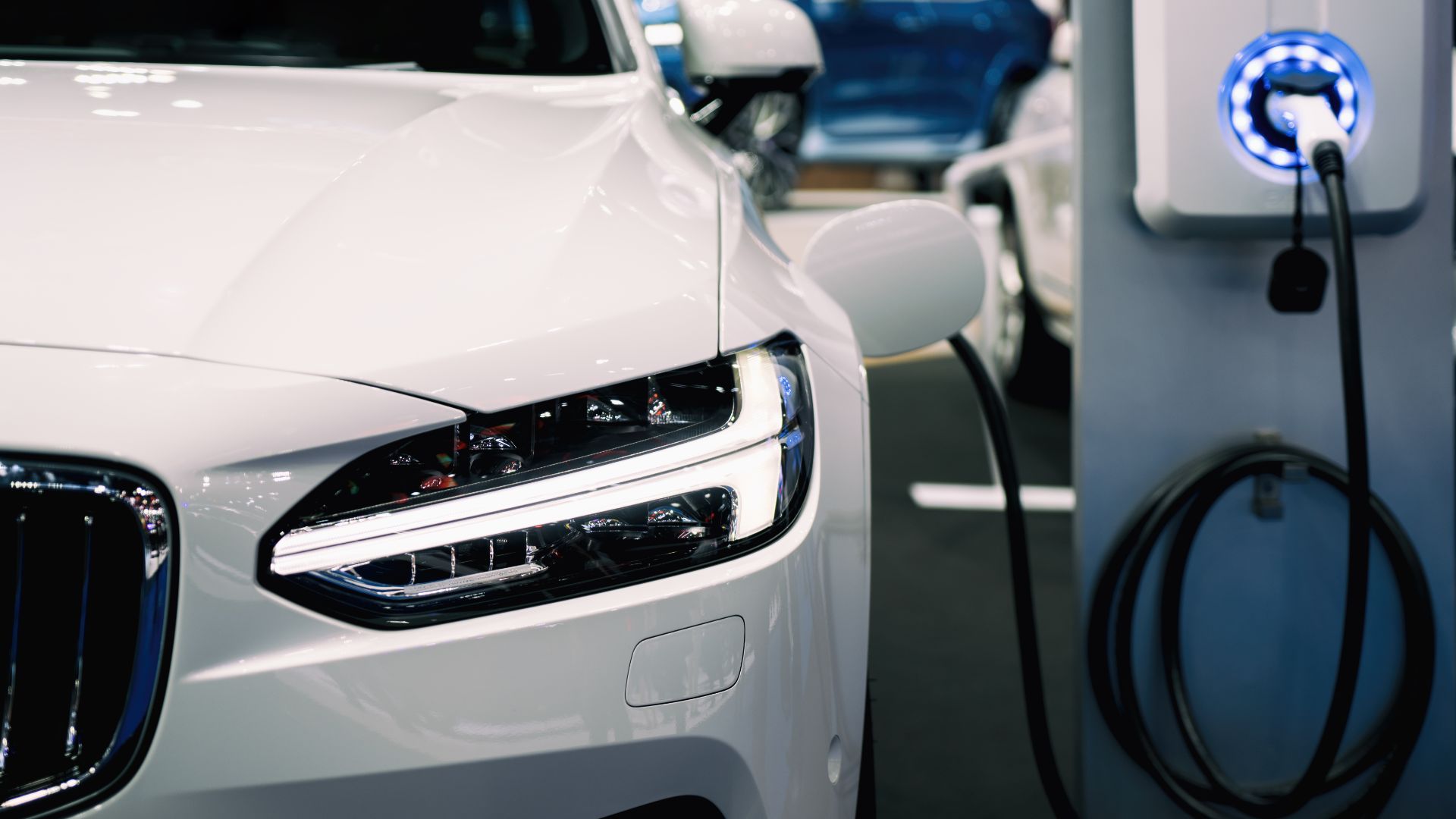 a white car plugged in to a charge station.|a close up of a parking meter with a building in the background.