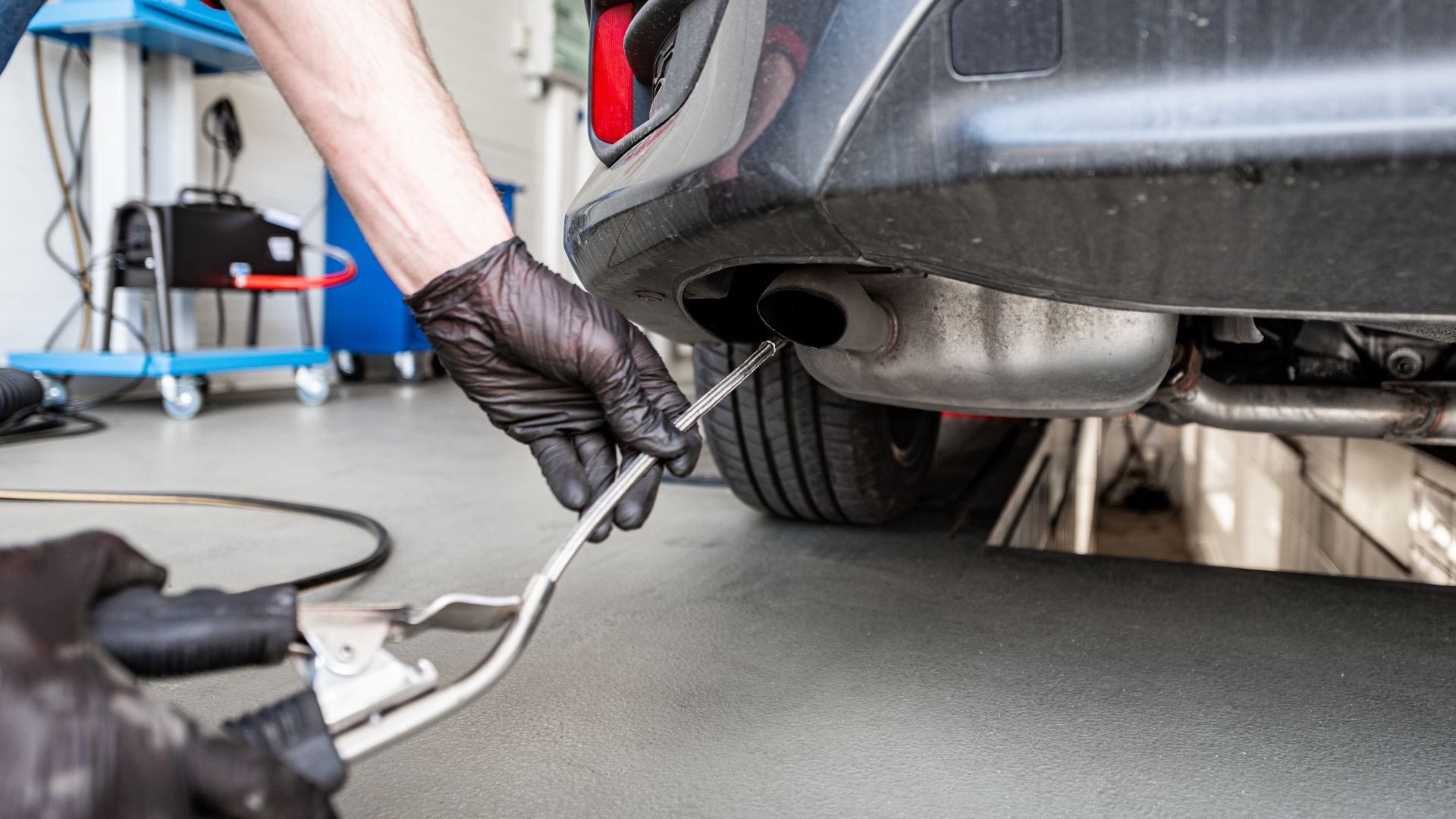 a man working on a car in a garage.|a close up of a person's hand holding a rusted pipe.