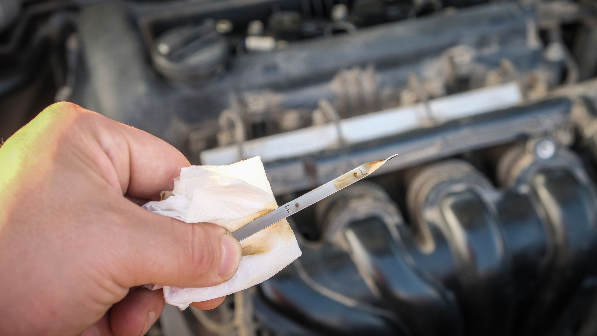 a person holding a pair of scissors in front of a car engine.|a car parked in a garage with a crack in the floor.