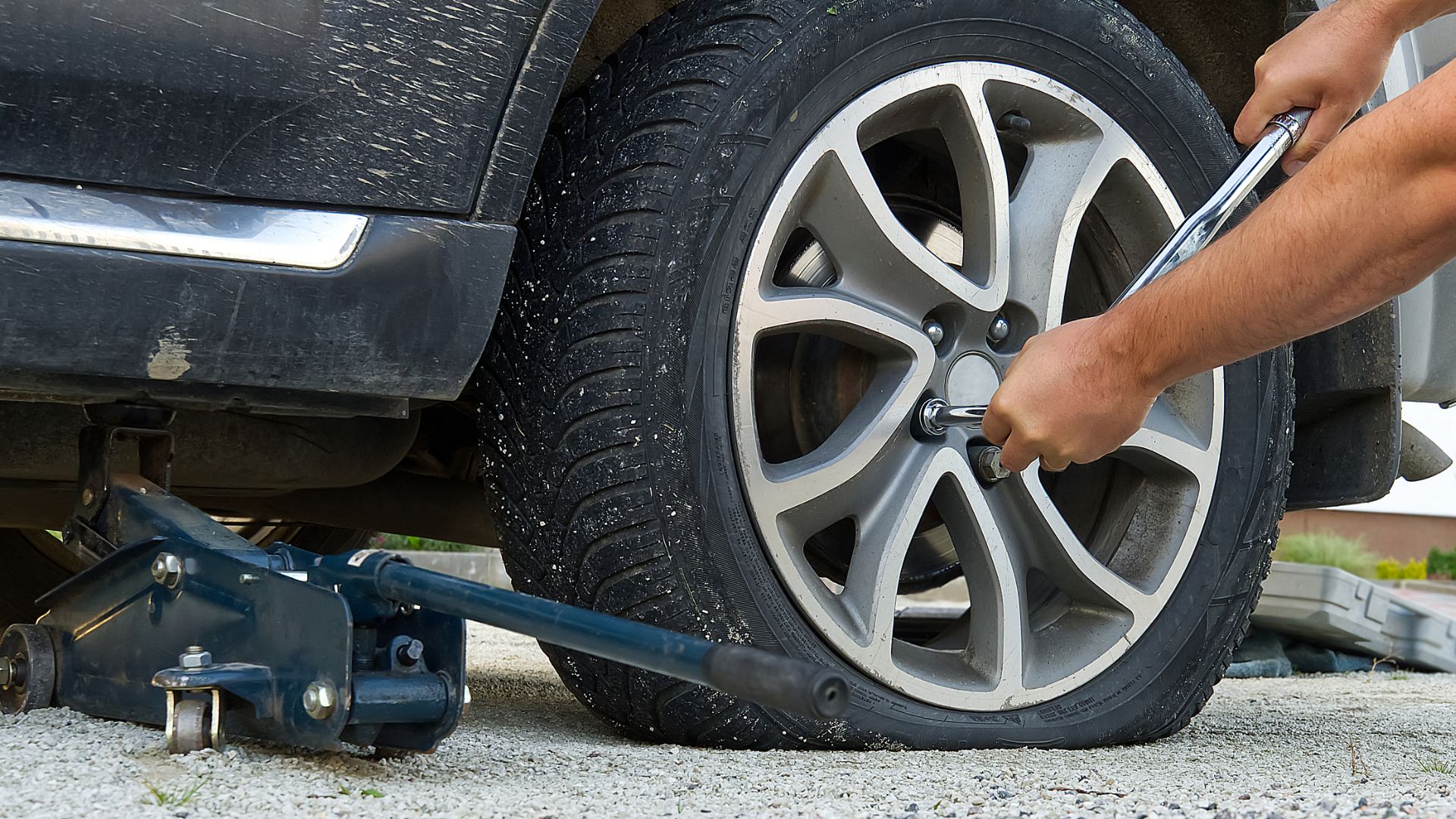 a man is changing the tire of a car.|the tire of a vehicle with a hose attached to it.