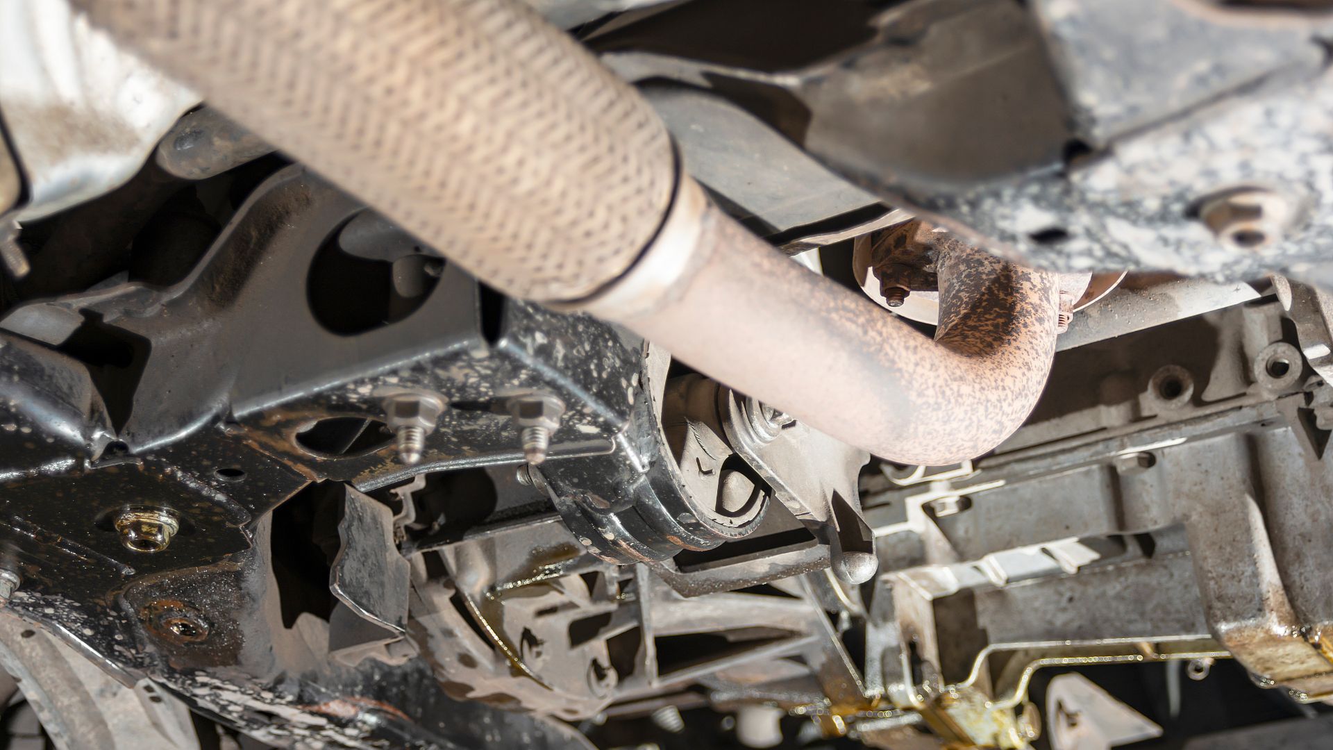 a close up of a metal object with a wrench.|a close up of a exhaust pipe on the ground.|two men working on a car in a garage.