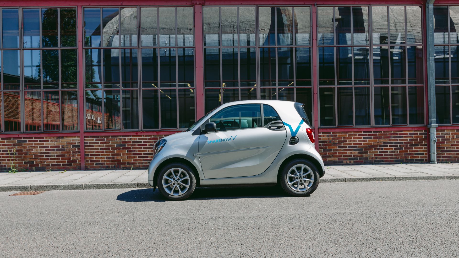 a smart car driving down a street next to other cars.|a smart car parked in front of a building.|a small car driving down a curvy road.