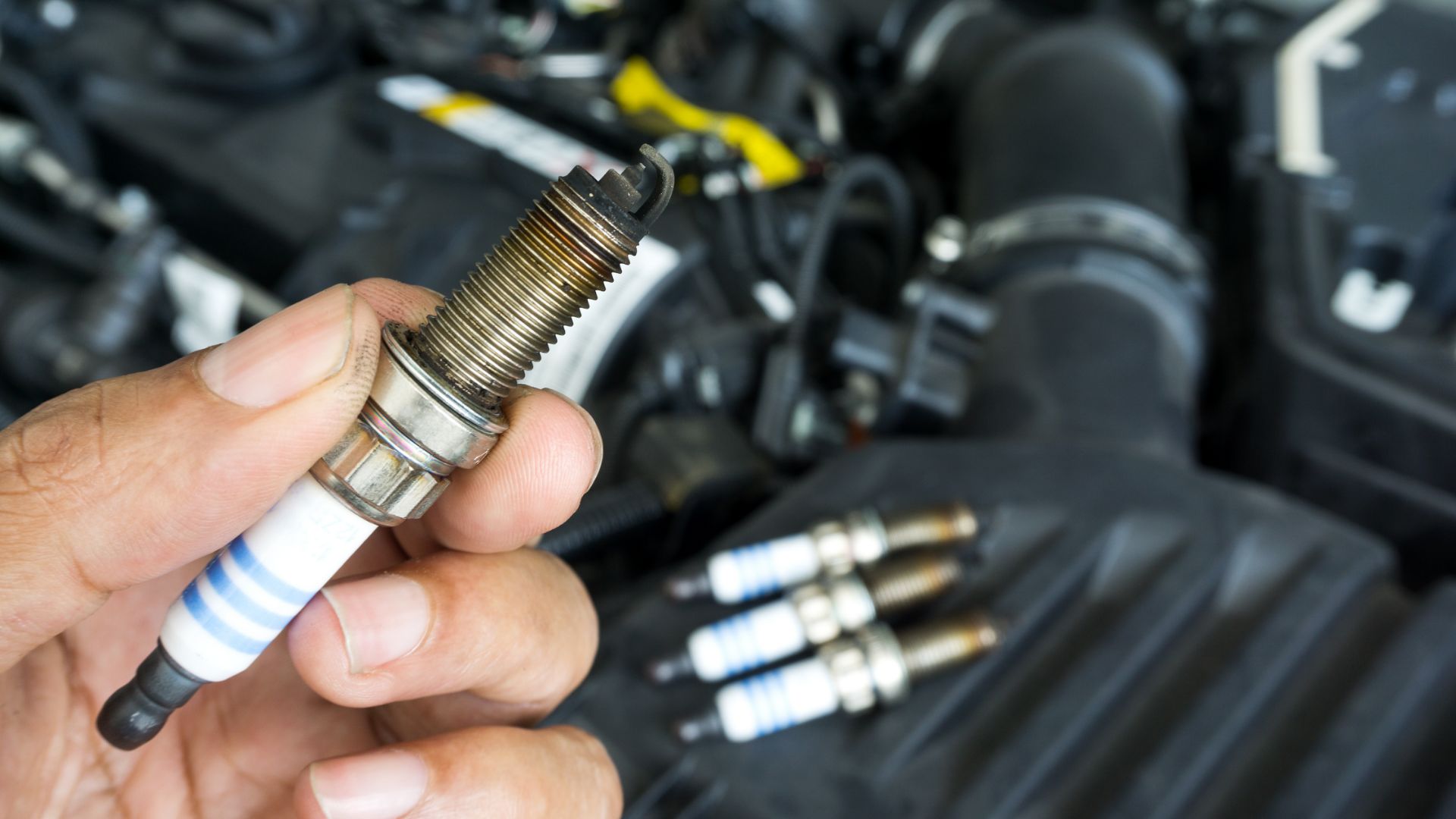 a man holding a spark in front of a car engine.|a close up of a person working on a motorcycle.|a close up of three sparks on a car engine.|a person is cleaning a car engine with a cloth.|a pair of gloves holding a wrench in front of a car engine.|a close up of a car's spark plugs and wires.|a person is working on a piece of metal.