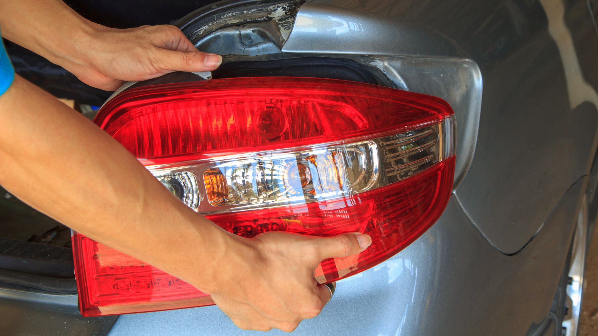 a person polishing the tail light of a car.|a close up of a car's tail light.|a man working on a car in a garage.