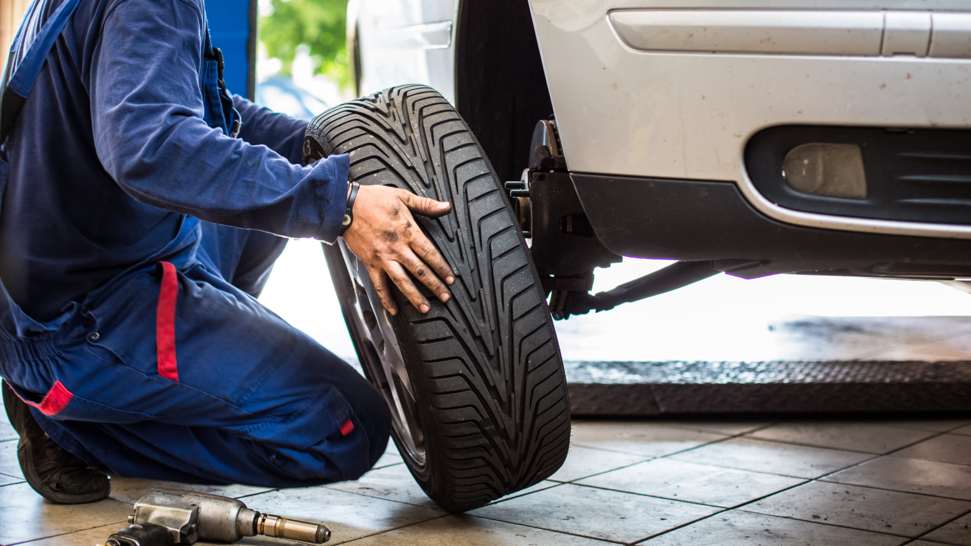 a man working on a tire with a wrench.|a person pointing at a tire on a car.|a man is working on a tire in a garage.