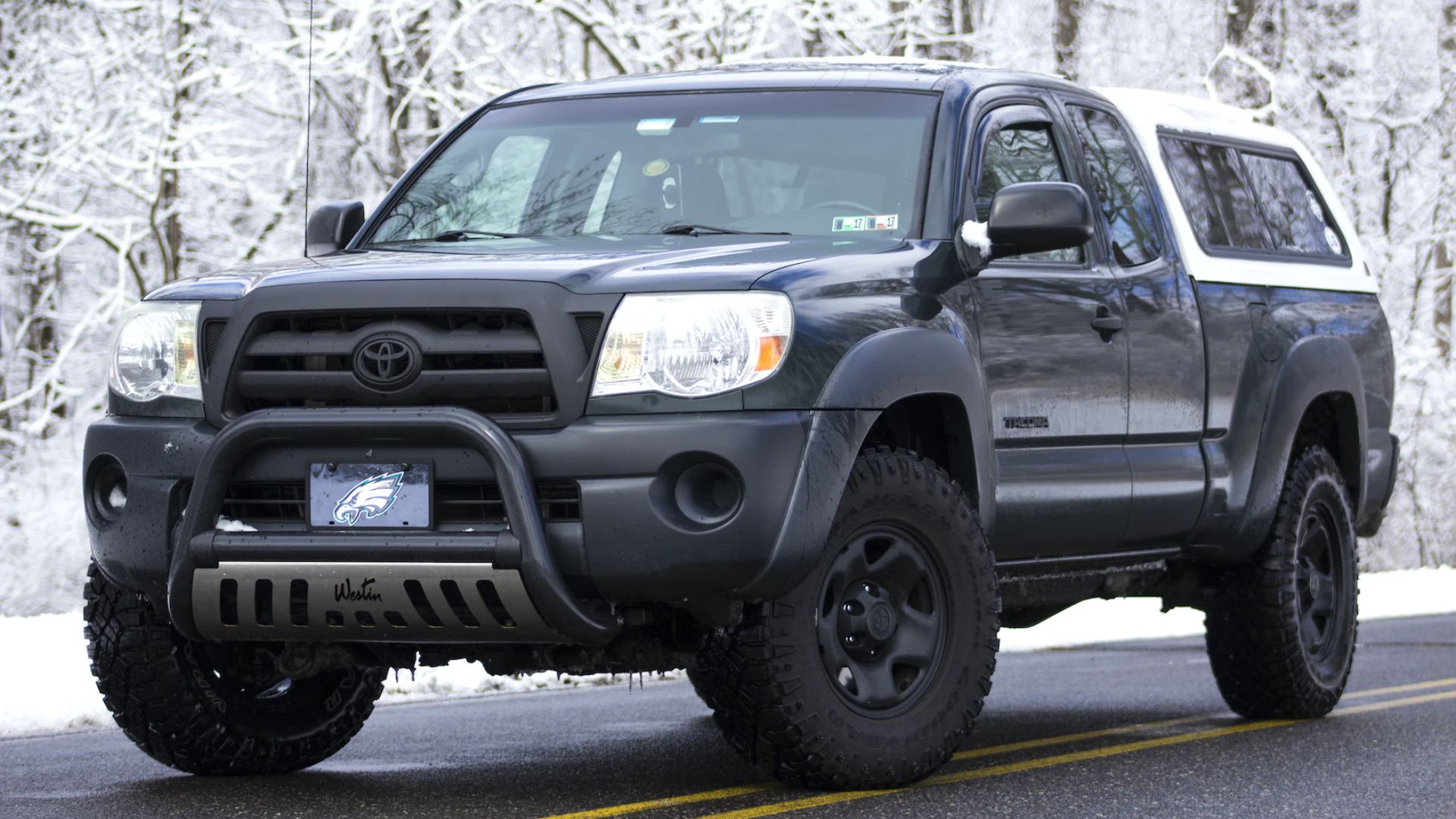 a black toyota truck driving down a road.|a tan toyota pickup truck parked on a dirt road.