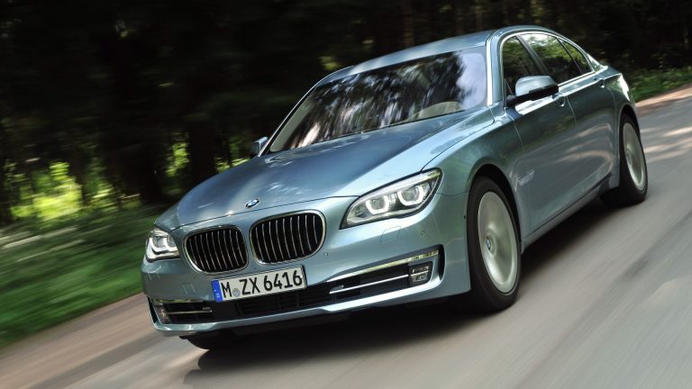 a silver car driving down a road next to a forest.