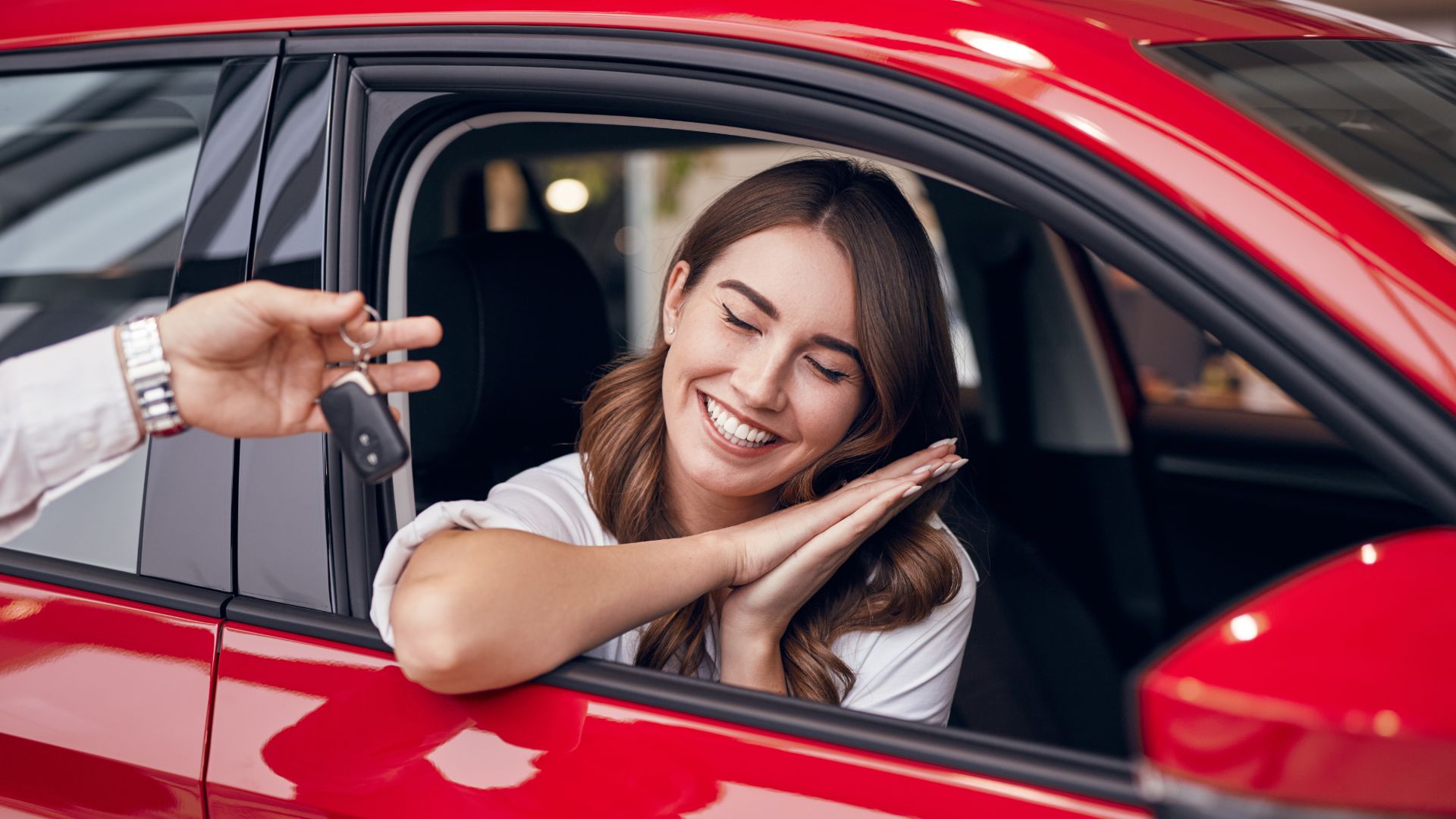 a woman is smiling while sitting in a red car.