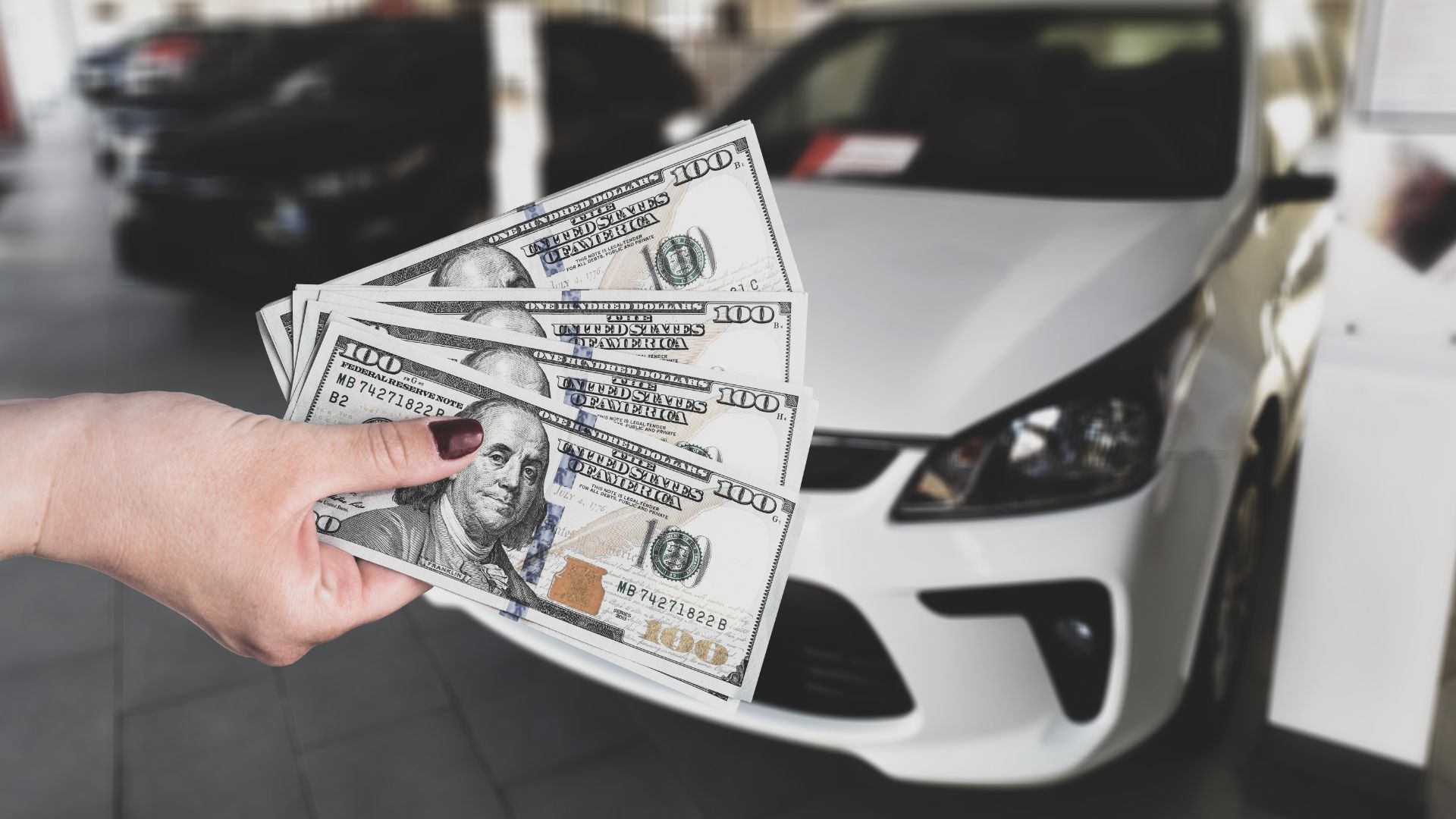 a person holding a bunch of money in front of a car.