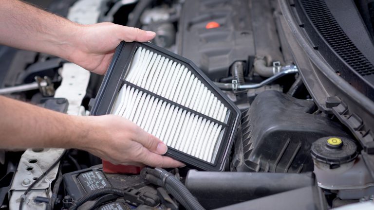 a man holding a air filter in front of a car.