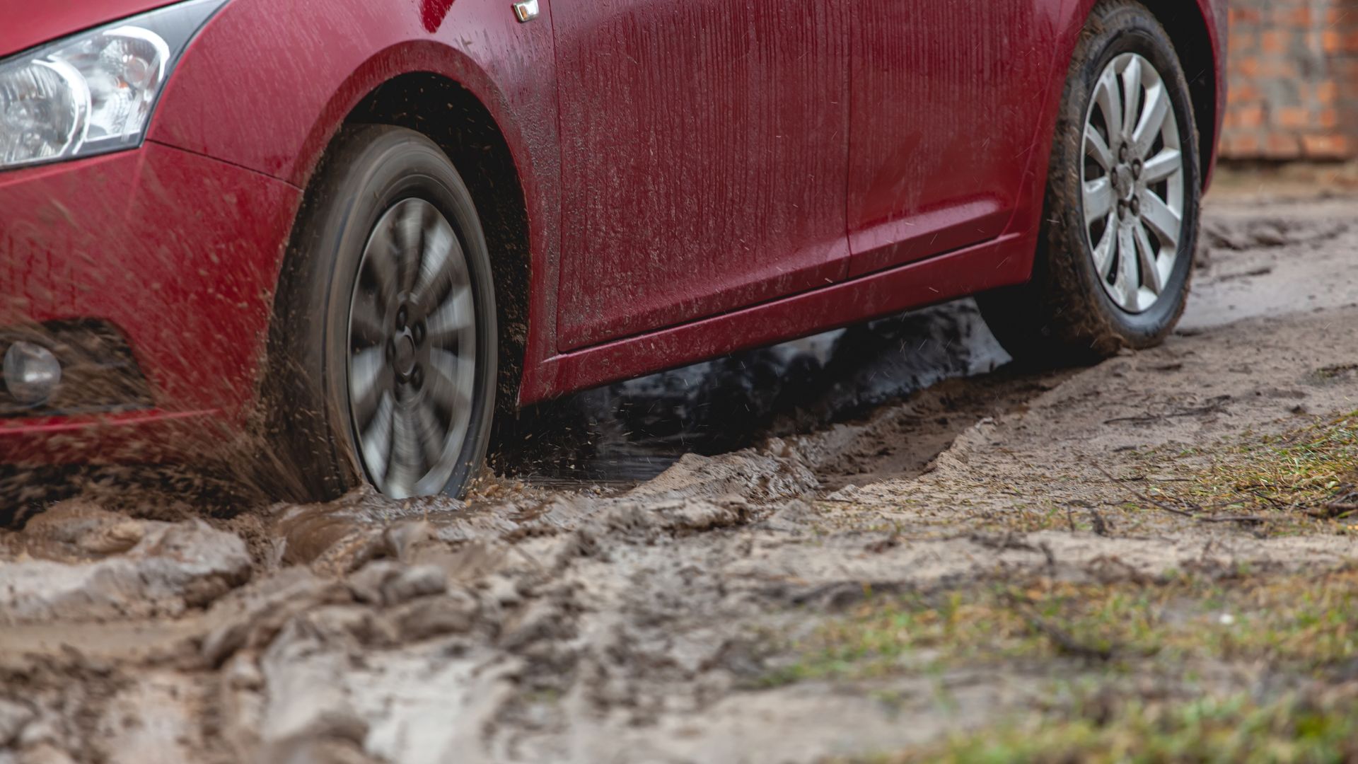 a red car driving through a puddle of mud.