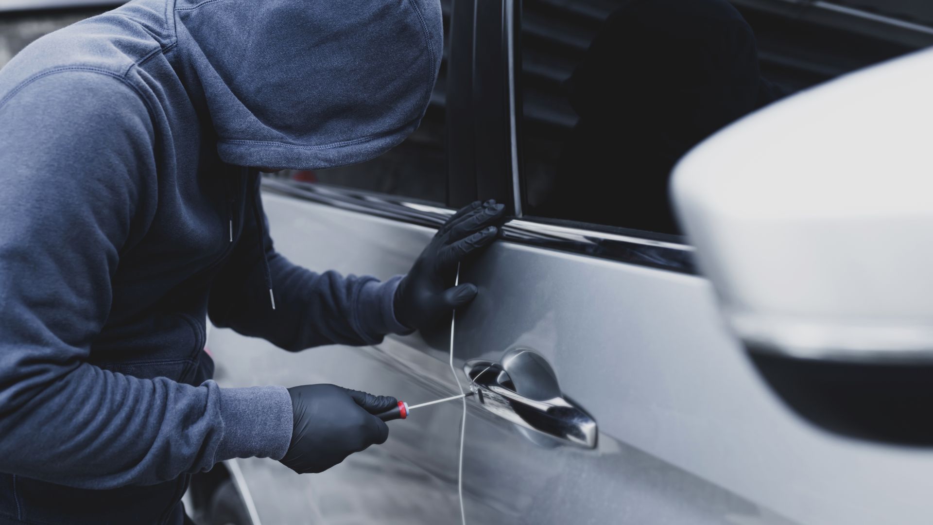 a person in a hoodie opening a car door.