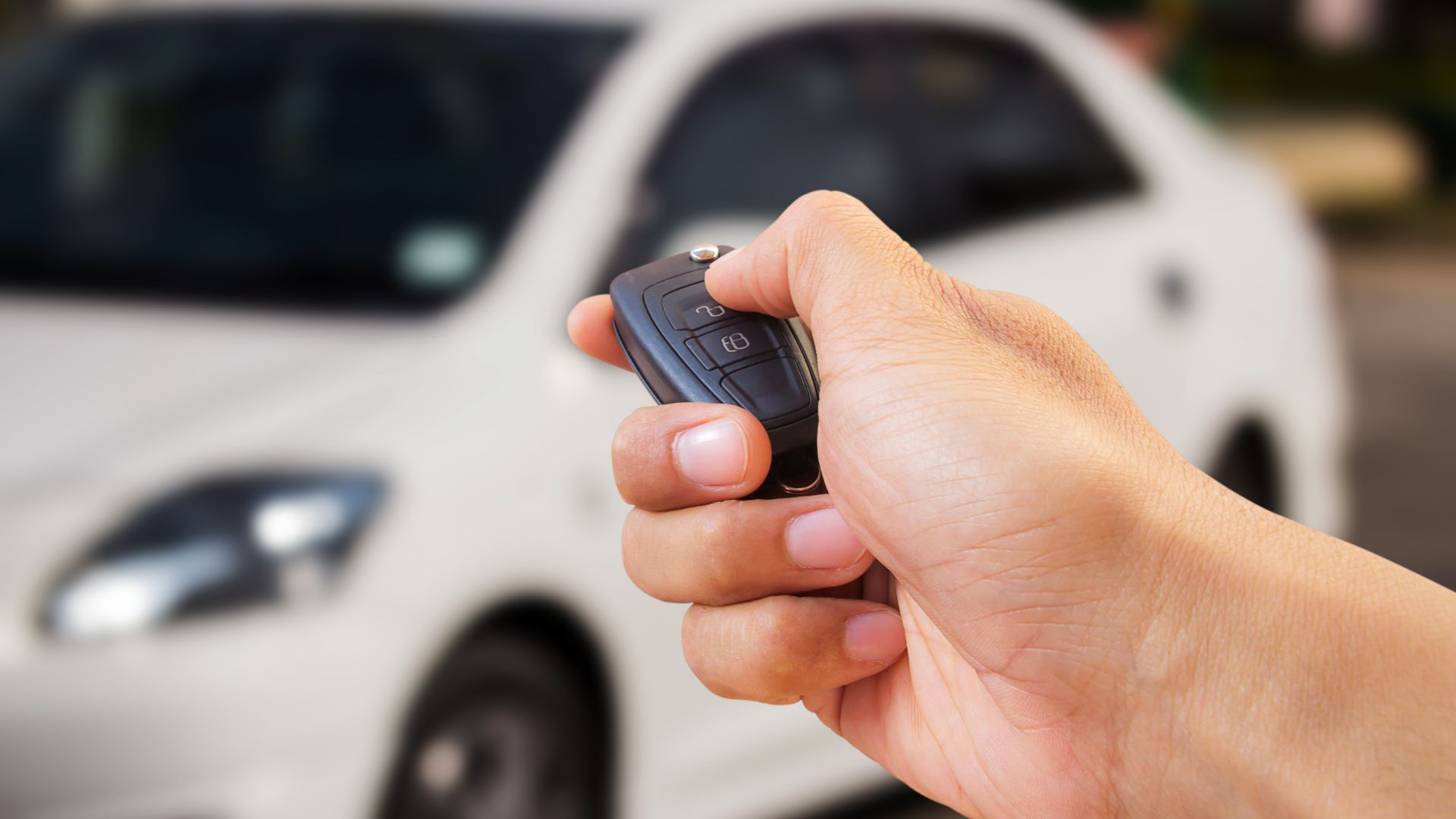a hand holding a cell phone in front of a white car.