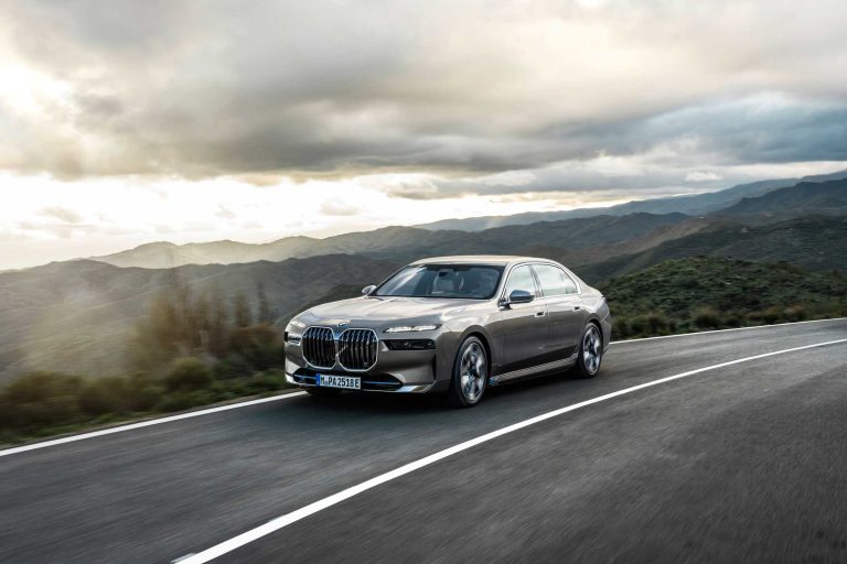 a silver car driving down a road with mountains in the background.