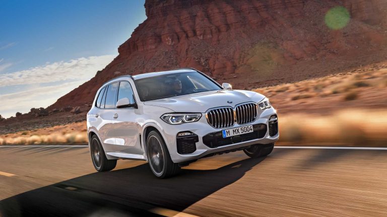 a white bmw x5 driving down a road.