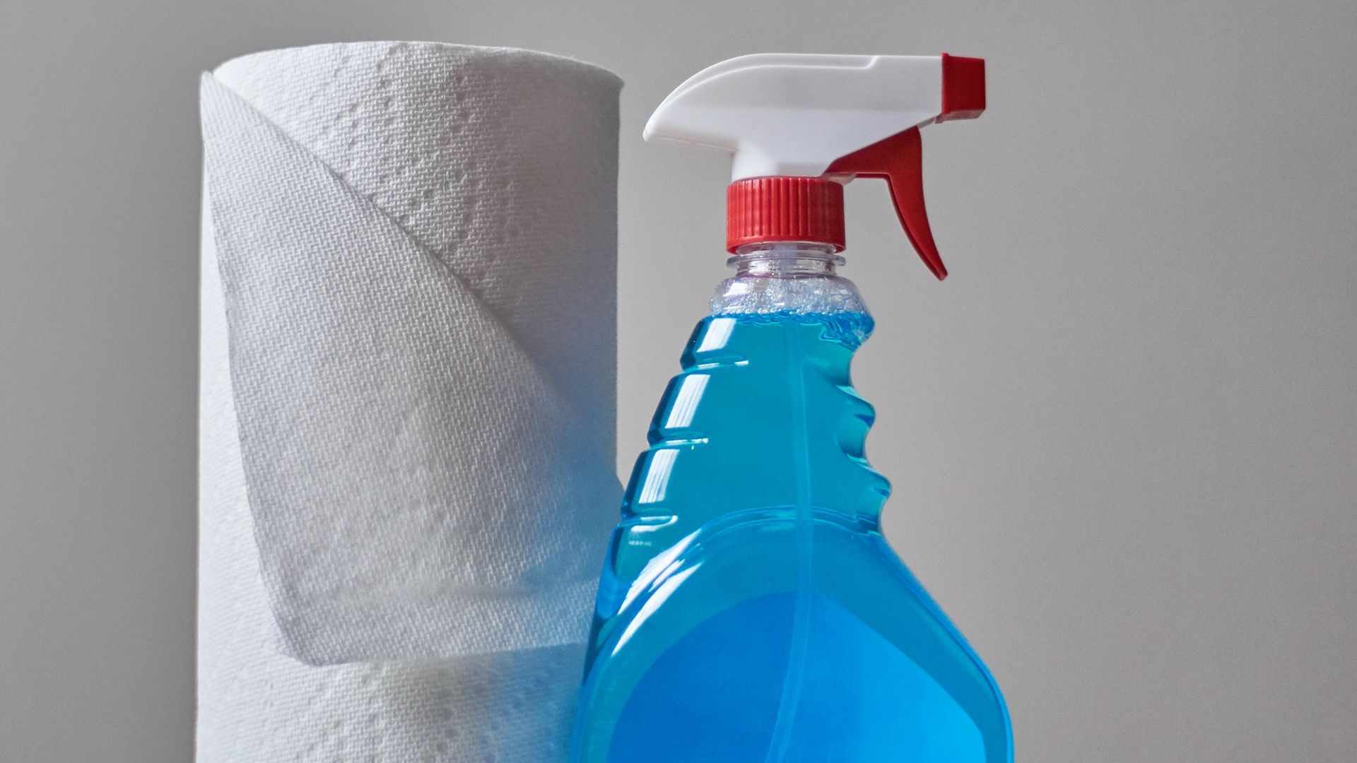 a bottle of cleaner next to a roll of toilet paper.