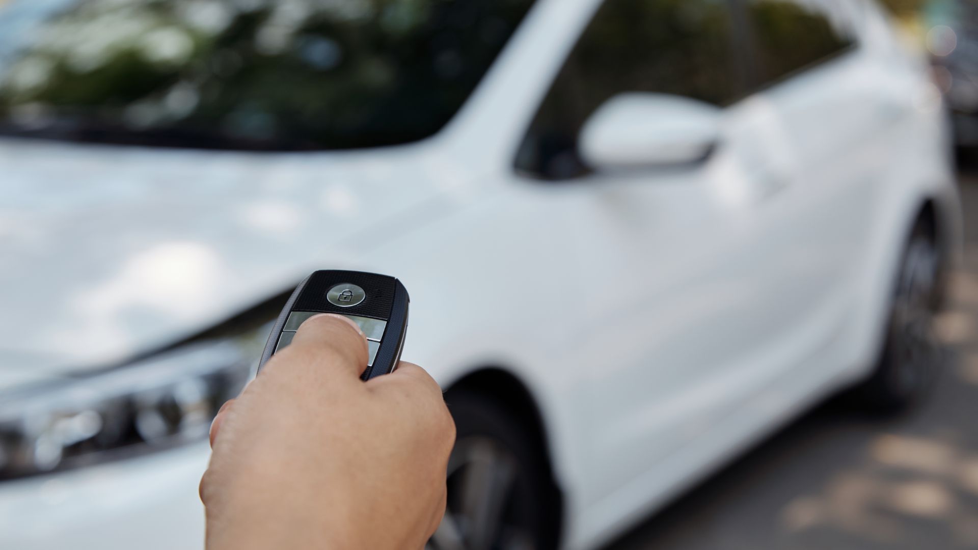 a person holding a cell phone in front of a white car.