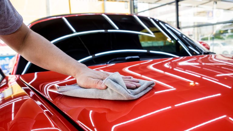 a person wiping down a red car with a cloth.