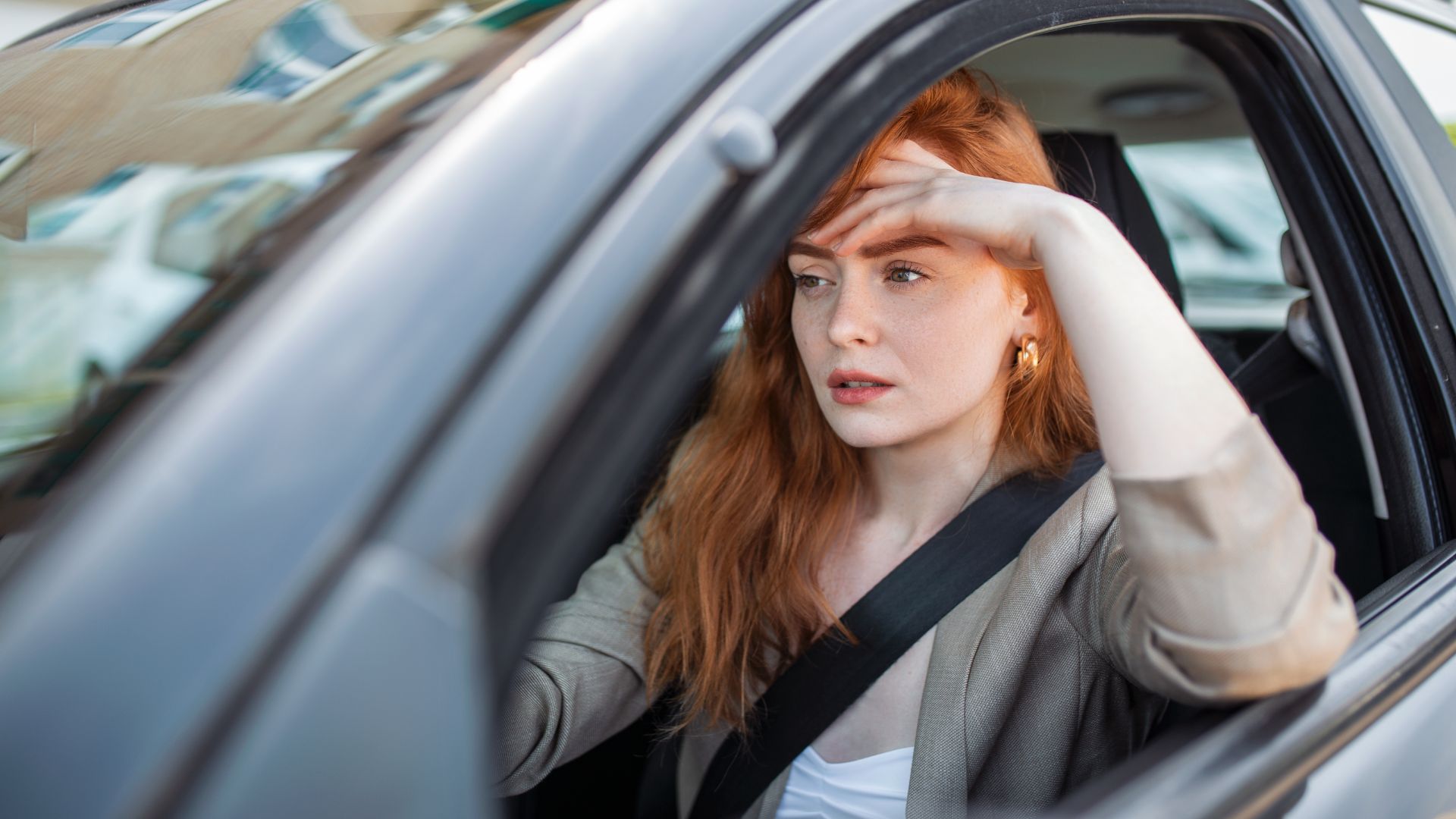 a woman sitting in a car with her hand on her head.