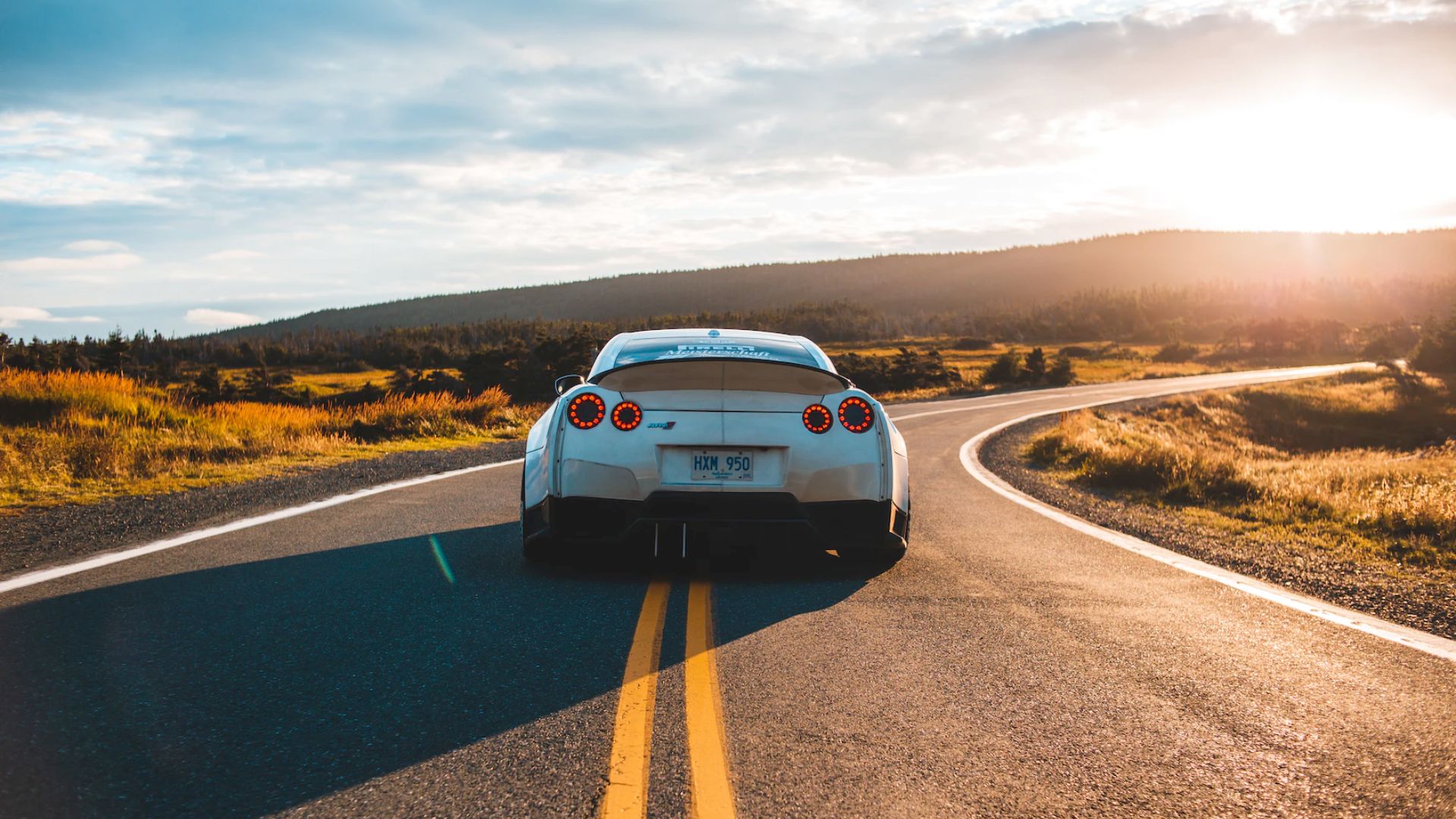 a white sports car driving down a country road.
