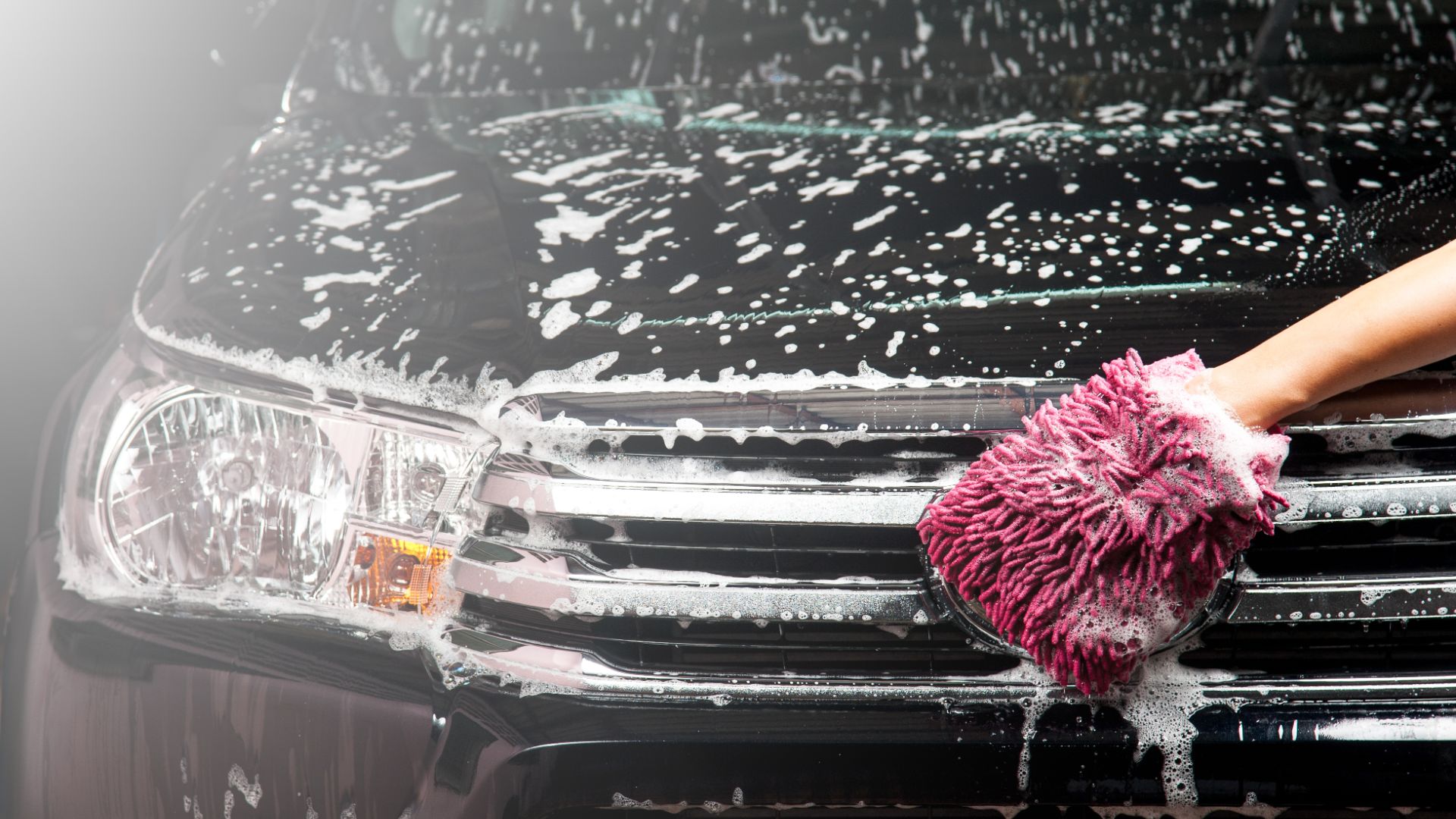 a person with a pink mitt on top of a black car.