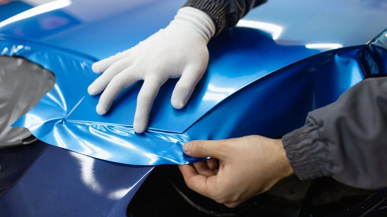 a person with a glove on top of a blue car.