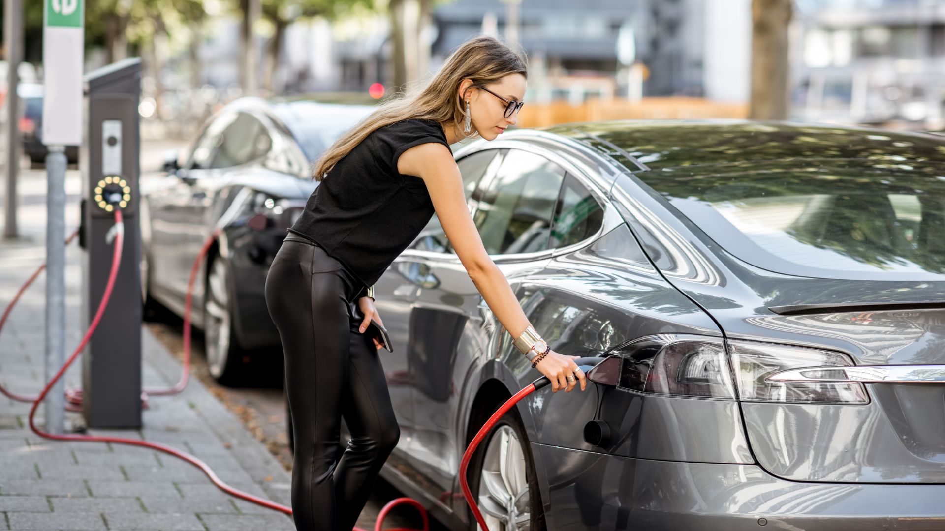a woman is charging her car on the street.