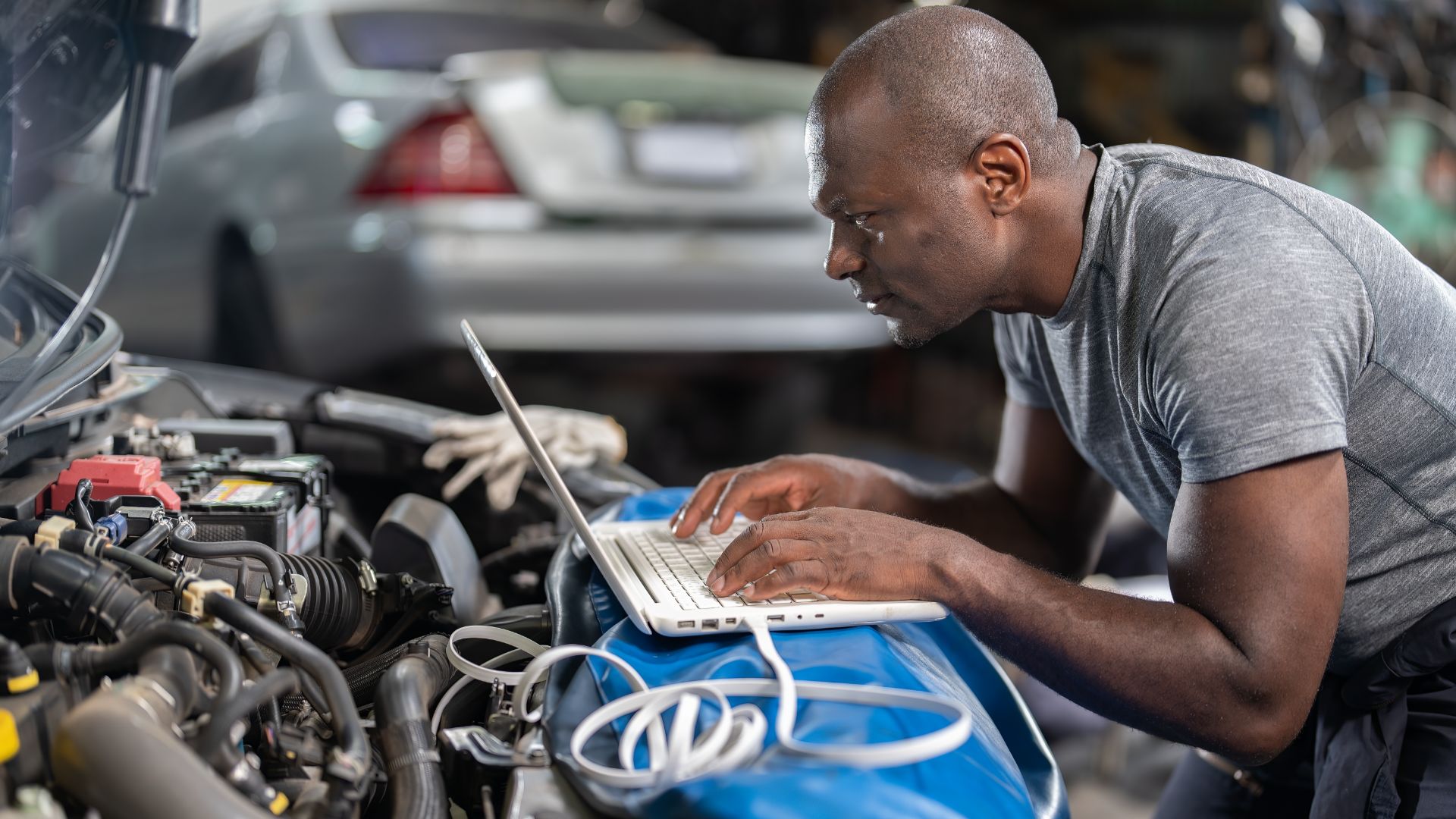 a man working on a laptop in front of a car.