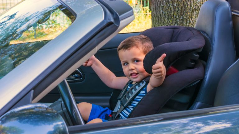 a little boy sitting in a car seat giving a thumbs up.