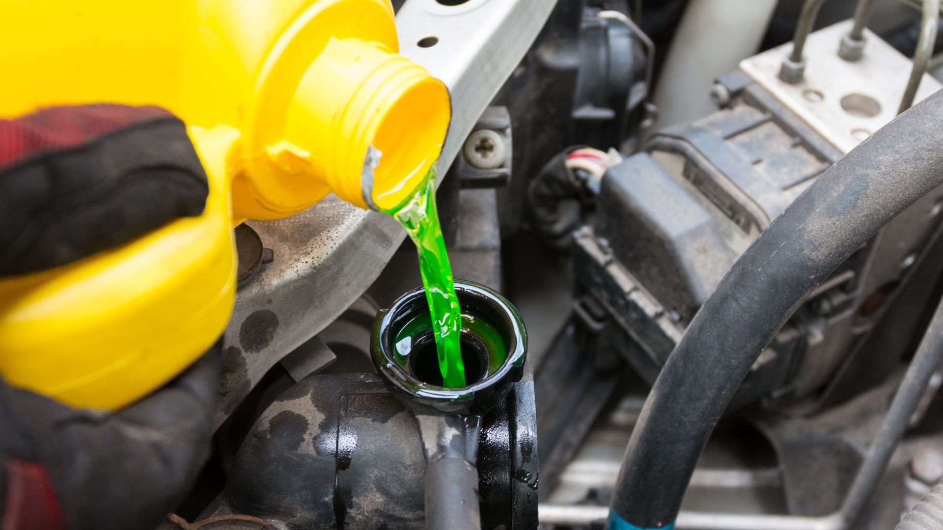 a person pouring a green liquid into a car's engine.
