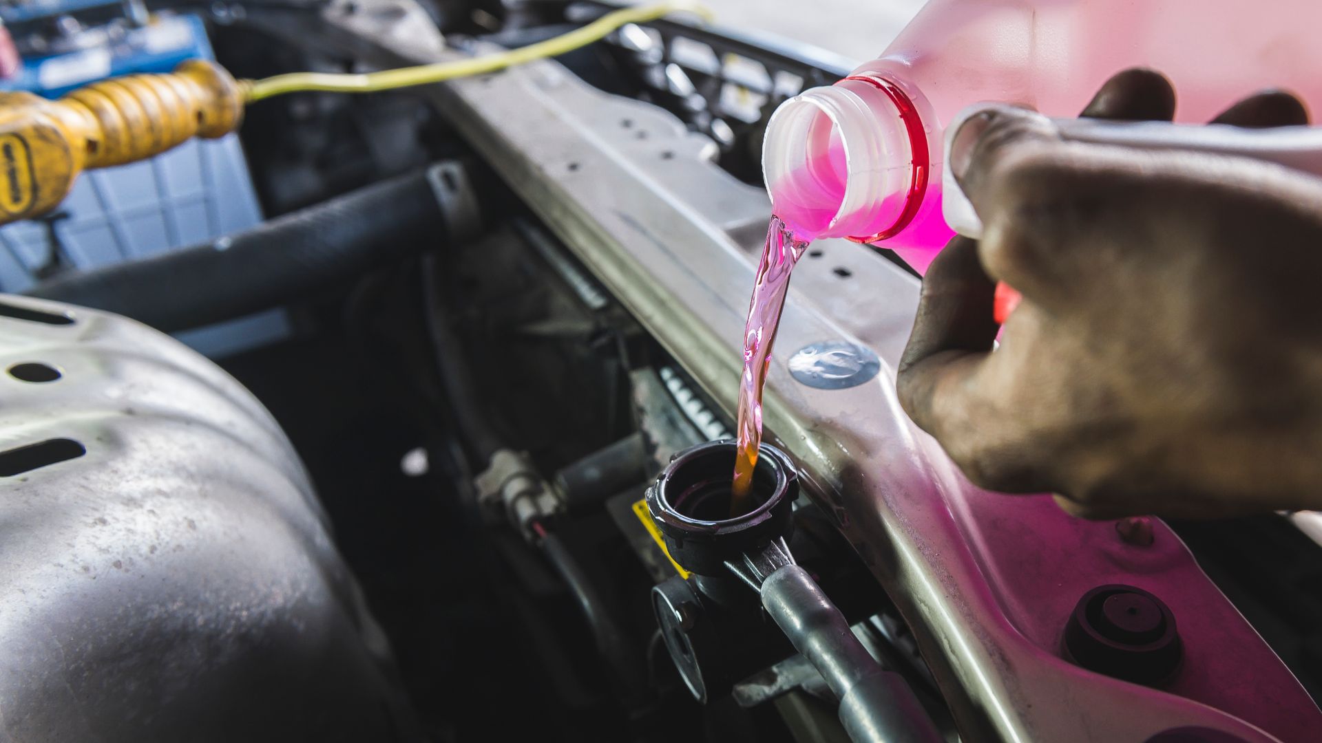 a person pouring a liquid into a car engine.