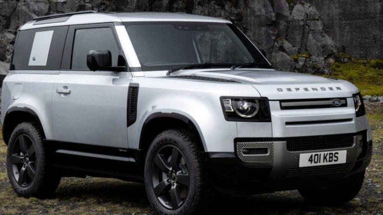 a silver land rover is parked in front of a rock wall.