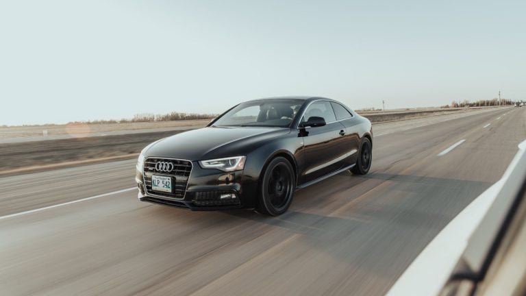 a black car driving down a highway with a sky background.