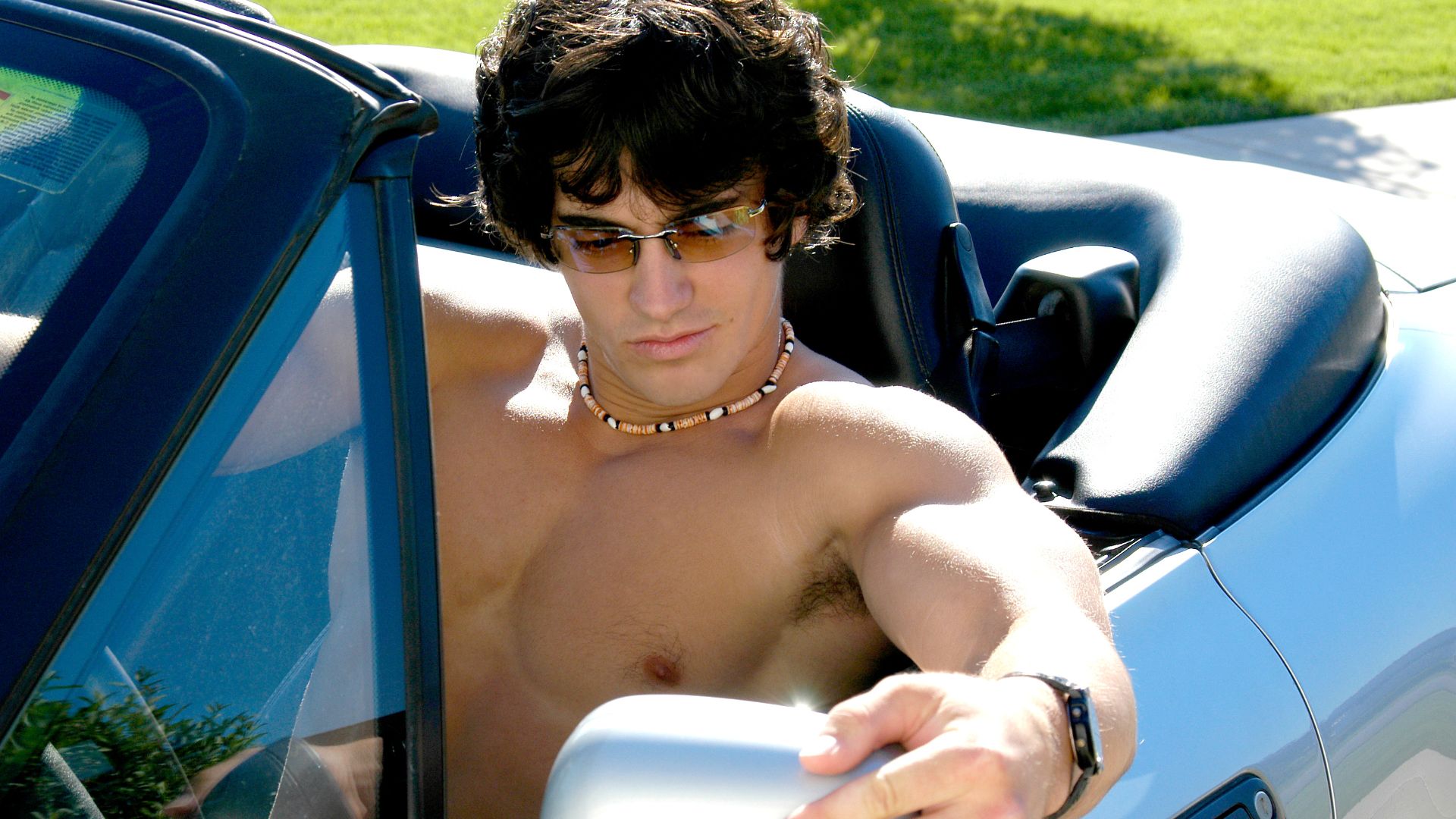 a shirtless young man leaning out of a car window.
