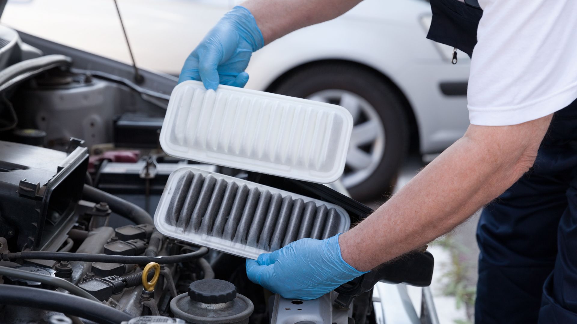 a man in a white shirt and blue gloves working on a car engine.