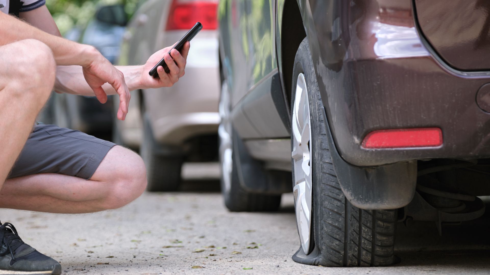 a man kneeling down next to a car holding a cell phone.