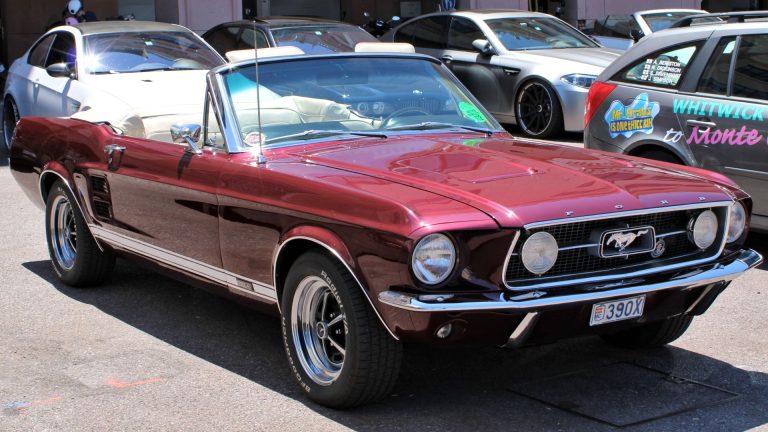 a red mustang parked in a parking lot next to other cars.