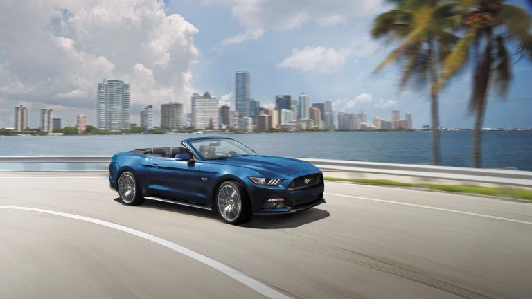 a blue mustang convertible driving down a road.