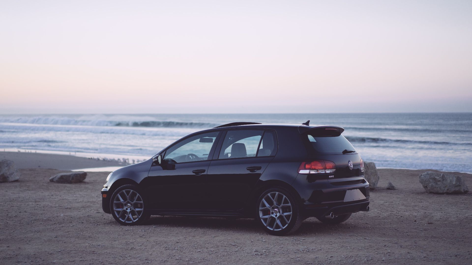 a black car parked on the beach near the ocean.