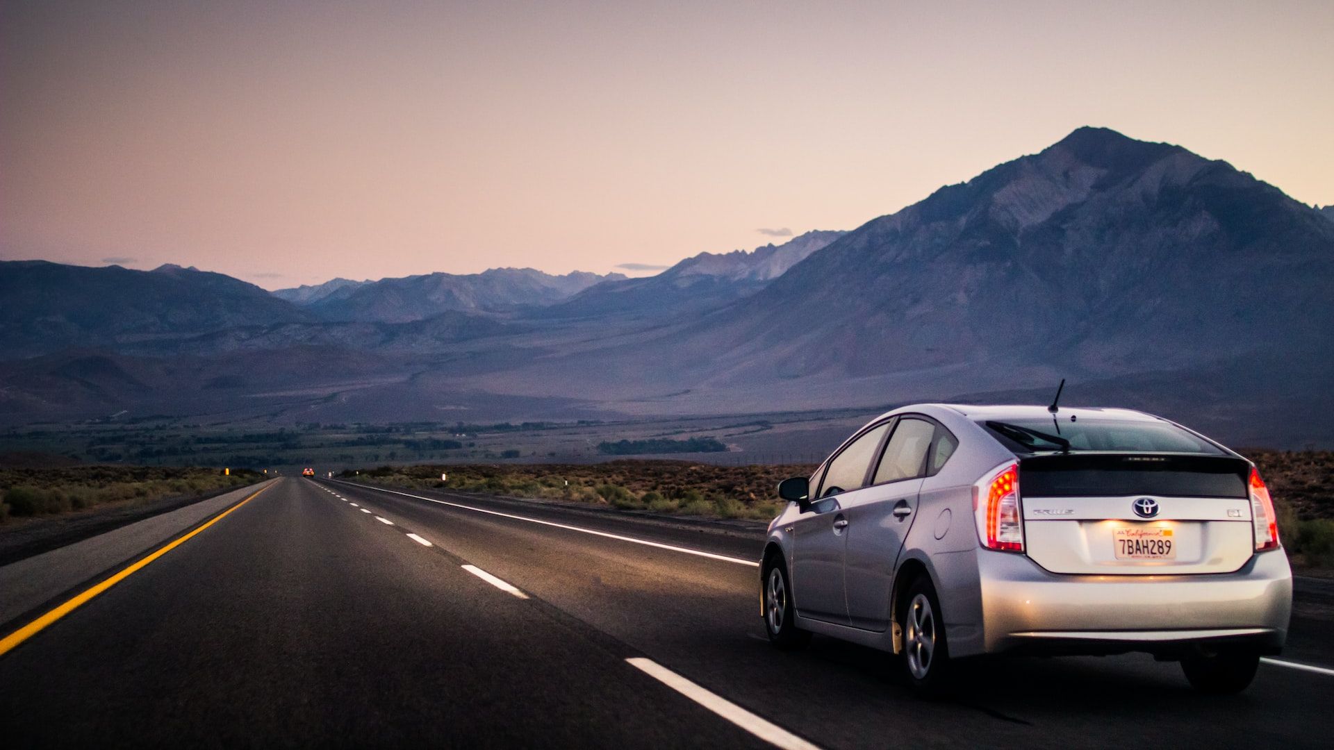 a car driving down a road with mountains in the background.