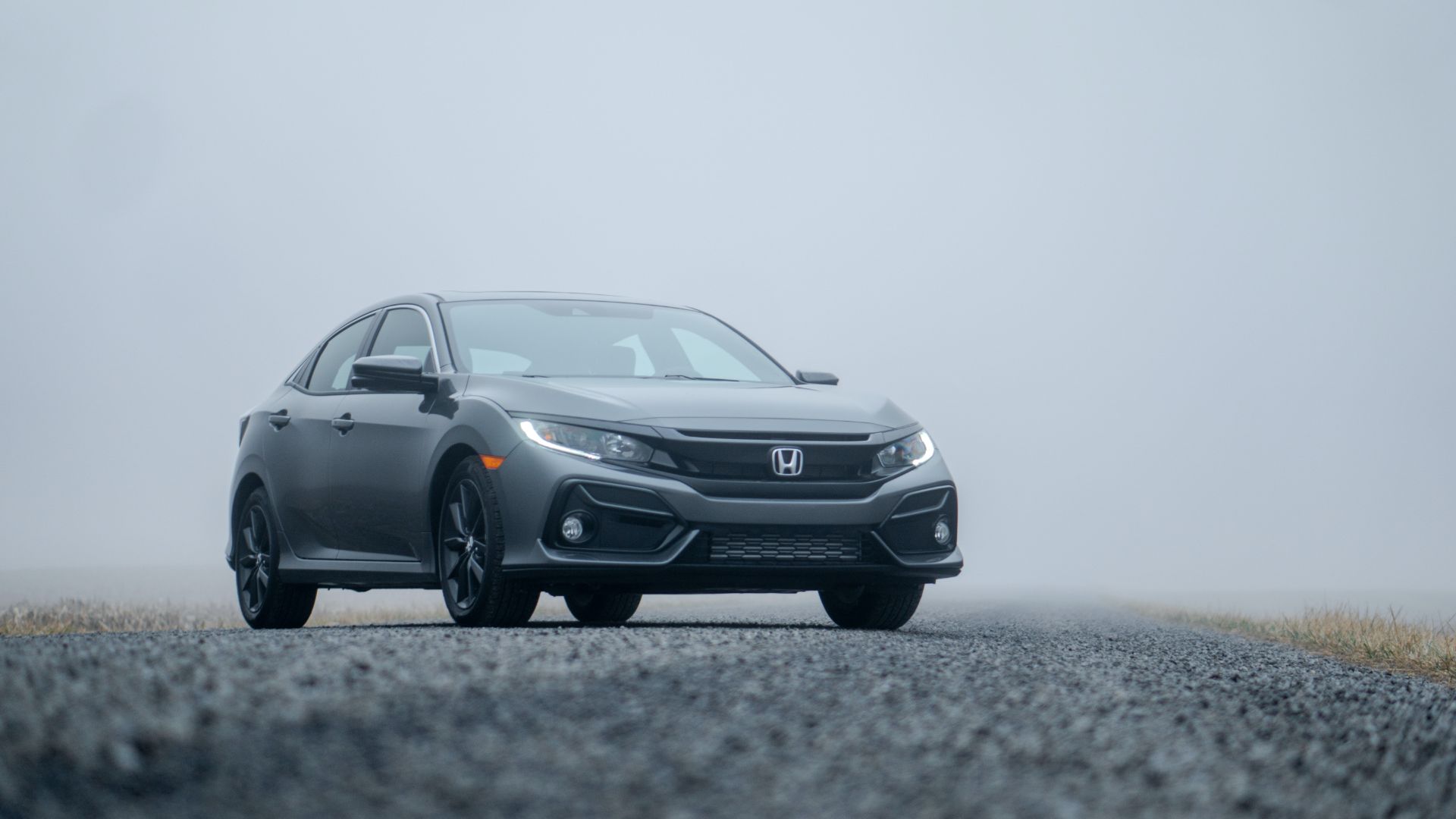 a gray car driving down a foggy road.