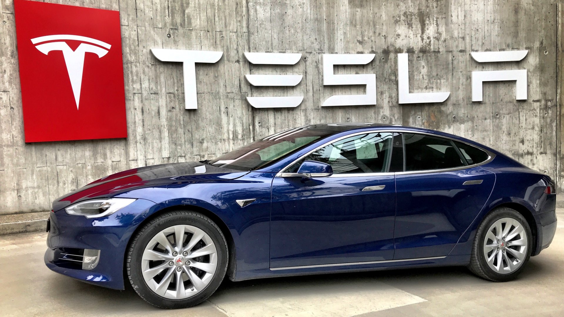 a blue tesla car parked in front of a tesla sign.