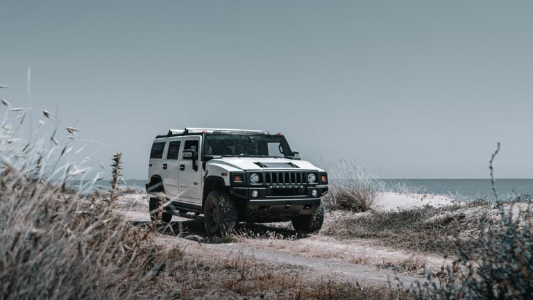 a white jeep driving down a dirt road next to the ocean.