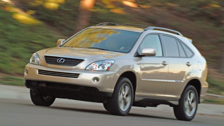 a silver suv driving down a street next to a forest.