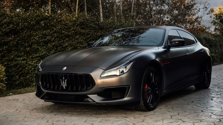 a black masera is parked in front of some bushes.