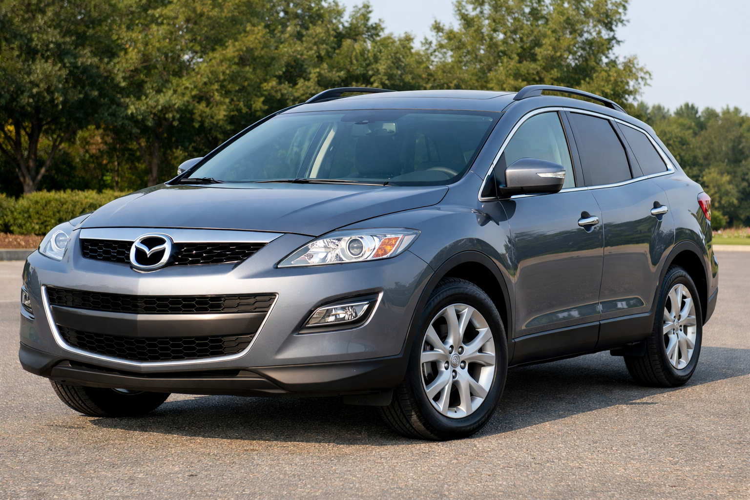 A gray Mazda CX-7 SUV is parked on an asphalt surface with green trees in the background, showcasing Mazda's signature style often seen in models like the Mazda CX-7—just be sure to research Mazda CX-7 years to avoid before buying used.