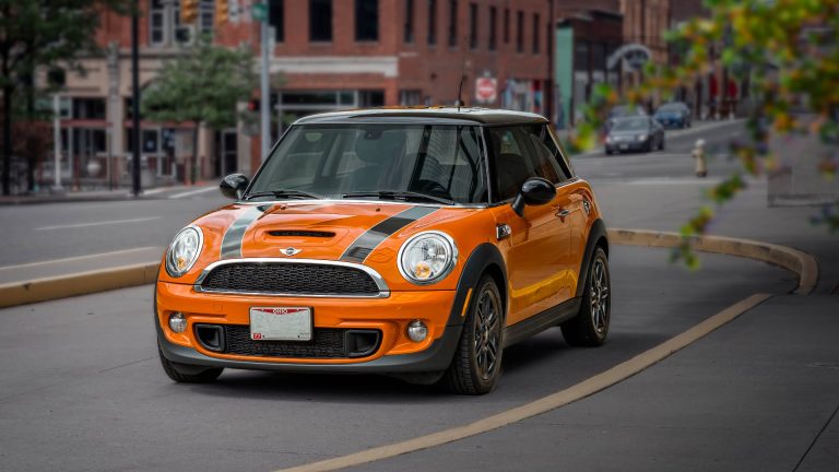 an orange and black mini car driving down a street.