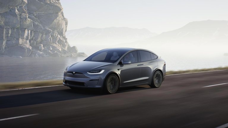 a silver car driving down a road next to a mountain.